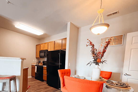 A kitchen with a black fridge and orange chairs.
