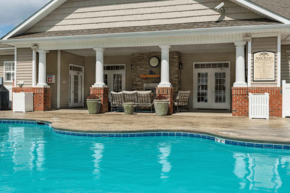 A pool in front of a house with a porch.