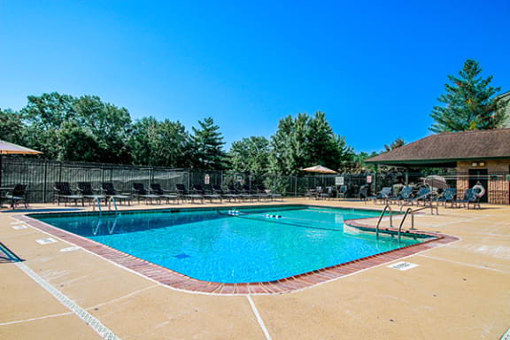 a swimming pool with chairs around it and trees in the background