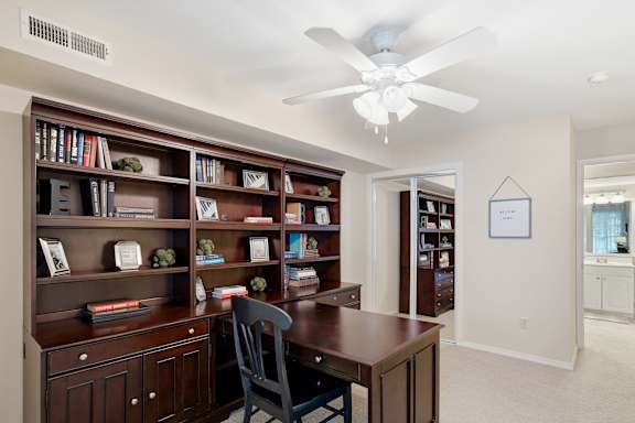 A room with a ceiling fan and a bookshelf filled with books.