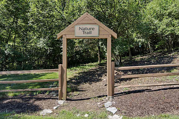 A wooden Nature Trail sign is in front of a wooded area.