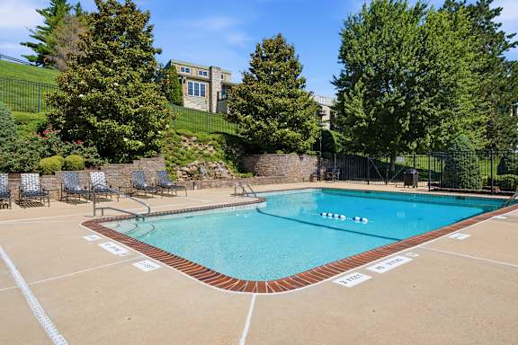 A large outdoor swimming pool surrounded by a fence and trees.