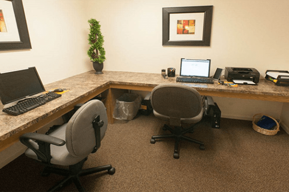 a desk with two computers and two chairs at the business center available at valley-stream