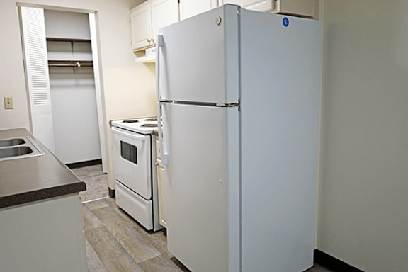 A white refrigerator stands in a kitchen with a sink and stove.