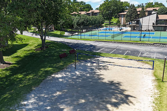 A tennis court is surrounded by a grassy area and trees.