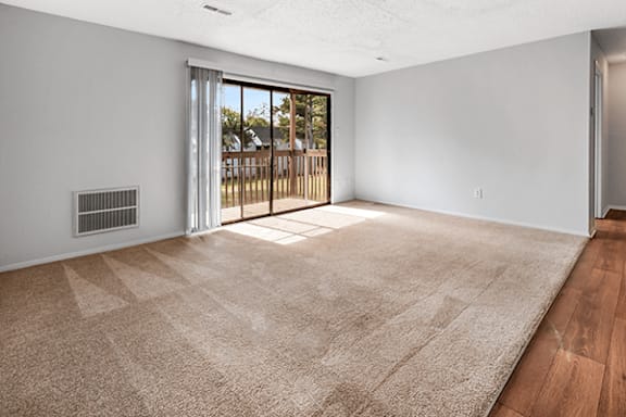 A room with a beige carpet and a sliding glass door leading to a deck.