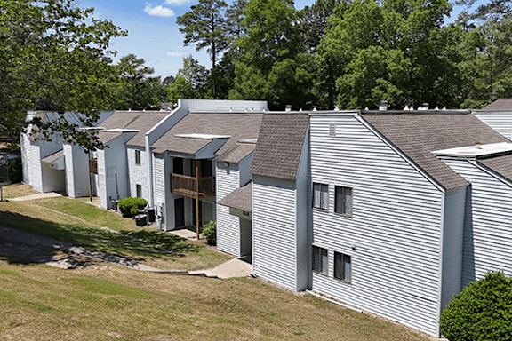 A white building with a grey roof is surrounded by trees.