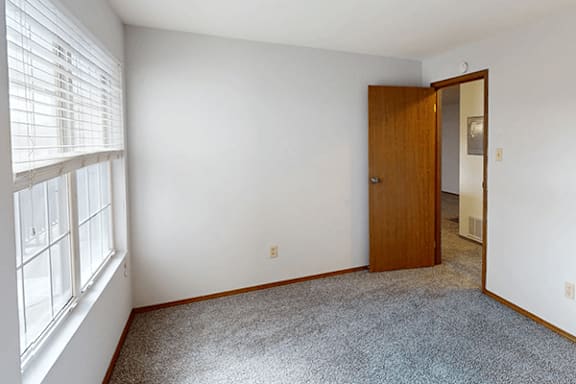 A room with a carpeted floor, a wooden door, and a window with blinds.