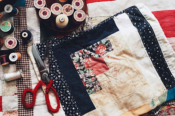 A quilted patchwork piece of fabric with a pair of scissors and spools of thread.