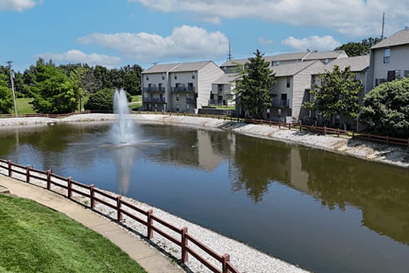 A fountain in the middle of a pond in front of apartment buildings.