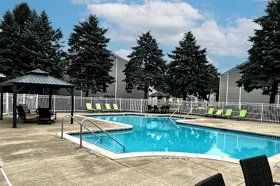 A pool surrounded by trees and chairs.