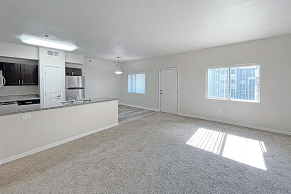 A sunny day in a spacious, empty living room with a kitchen area.