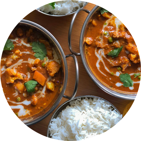 A dish of curry with rice and a bowl of curry with rice in the background.