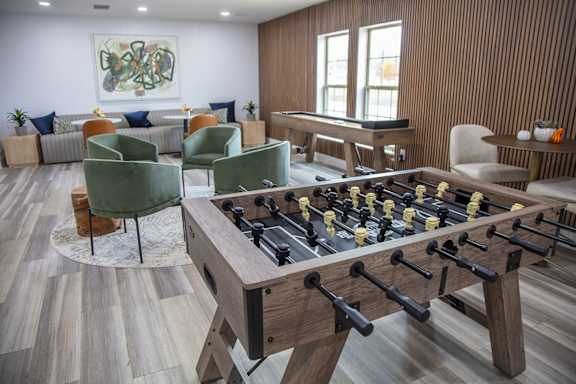 A foosball table is in the middle of a room with a pool table and couches.