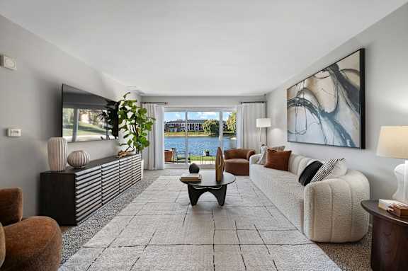 A spacious living room with a large window overlooking the water.