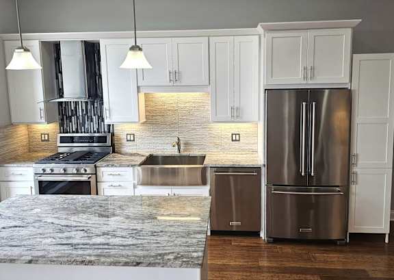 A modern kitchen with a stainless steel refrigerator and a marble countertop.