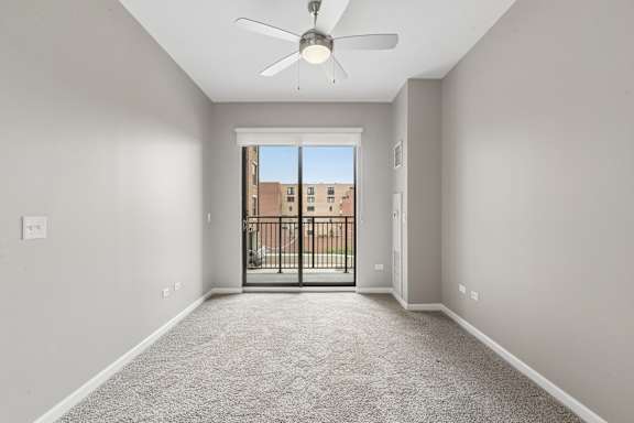 A room with a ceiling fan and a door leading to a balcony.