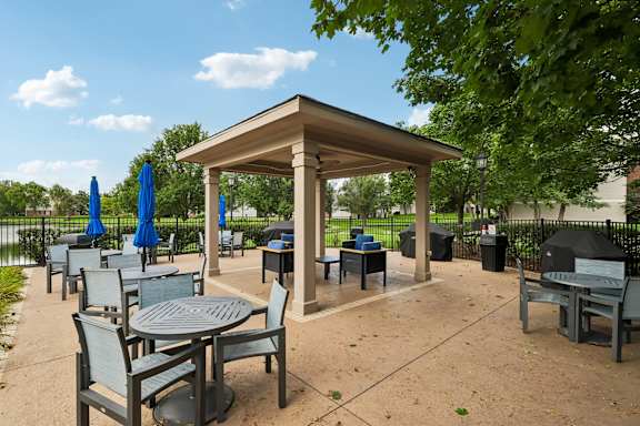 A gazebo with a table and chairs is surrounded by trees.