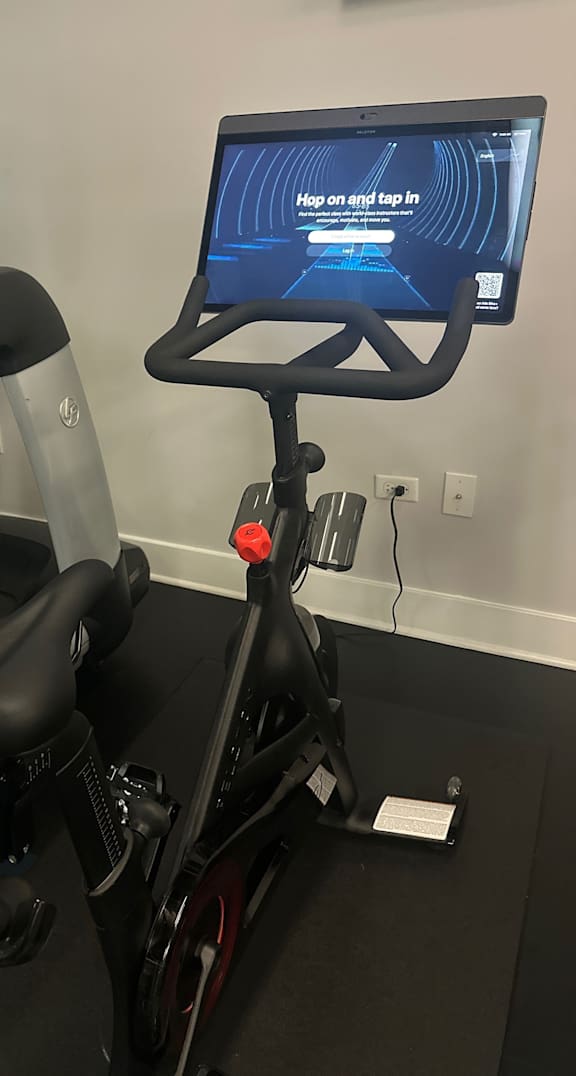 A stationary bike with a screen on the handlebars that says "Hop on and tap in".