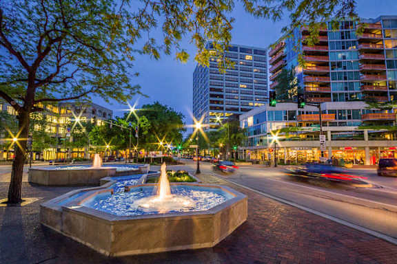 A city street at night with a fountain in the foreground.
