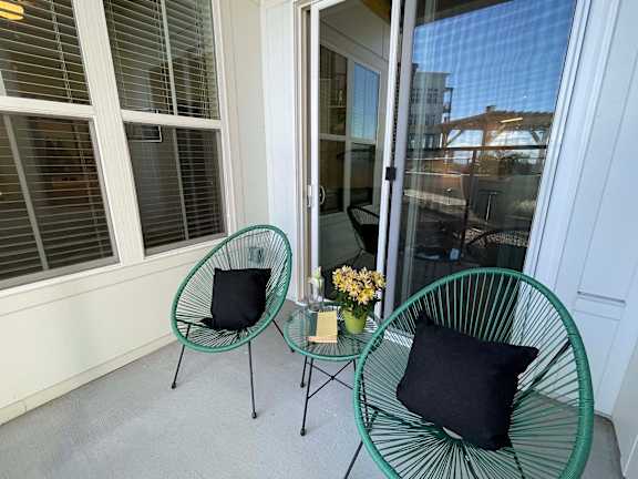 Two green chairs with black pillows are on a patio.