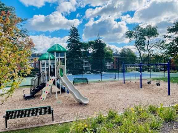 A playground with a green slide and a black bench.