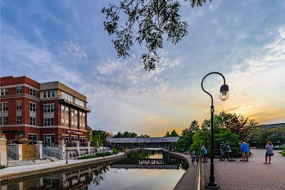 A sunset view of a river with people walking along the side.