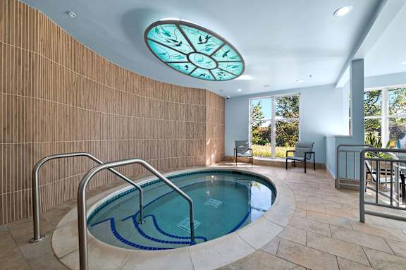 A round window with a clock on the wall above a swimming pool.