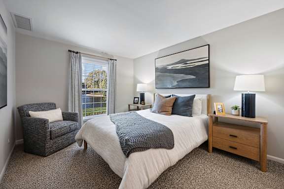 A bedroom with a large bed, a chair, and a painting on the wall.