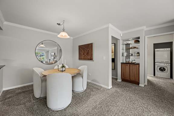 A modern living room with a round table and chairs, a mirror, and a view of the kitchen in the background.