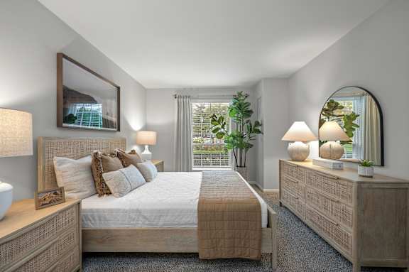 A well-lit bedroom with a large bed, a nightstand with a lamp, and a mirror on the wall.