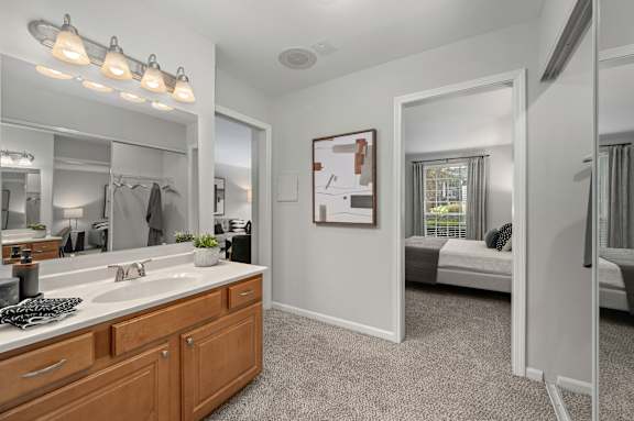 A bathroom with a vanity, mirror, and a bed in the background.