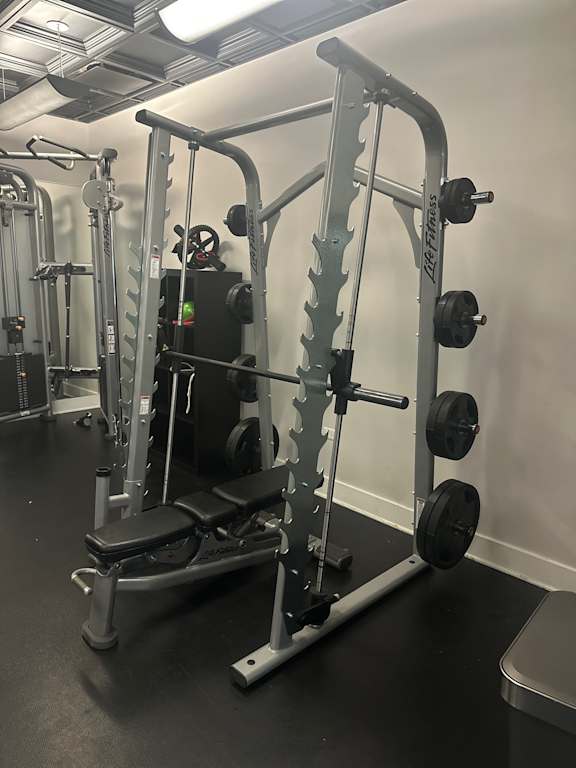 A black and white photo of a gym with a weight bench and a barbell.
