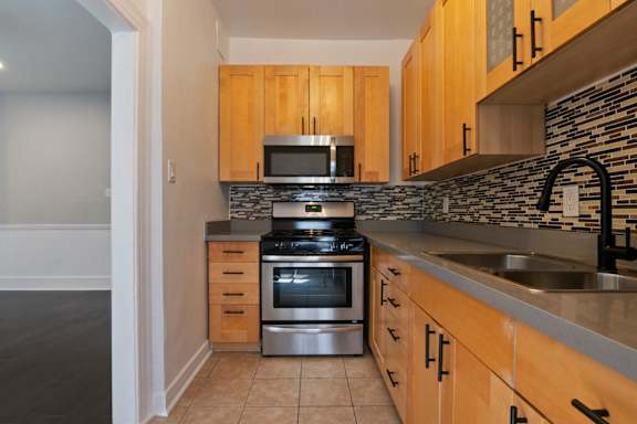 A kitchen with wooden cabinets and a stone backsplash at Brookmore Apartments Pasadena, CA