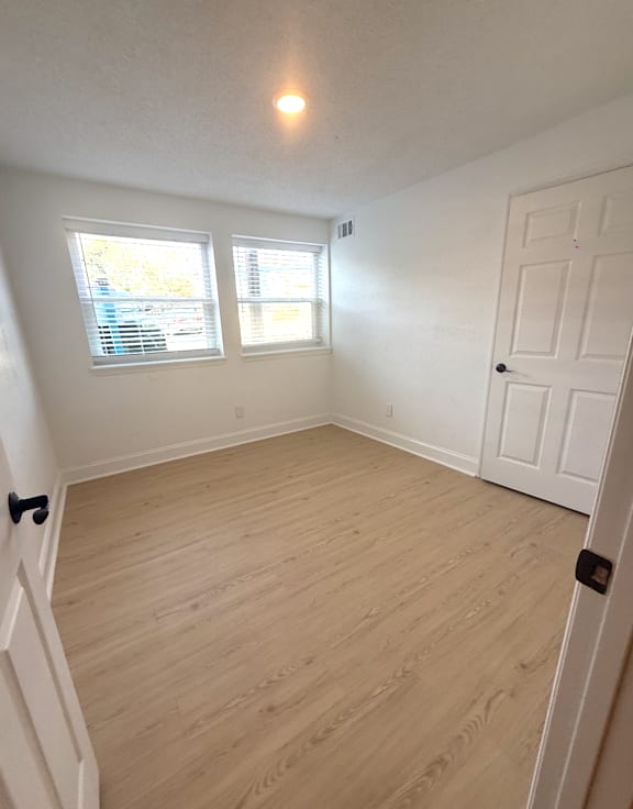 A room with a white door and two windows with blinds.