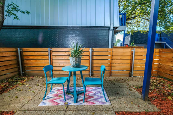 Patio on Stadium 700 ground-floor apartment in Arlington, TX with blue bistro table and tall privacy fence.
