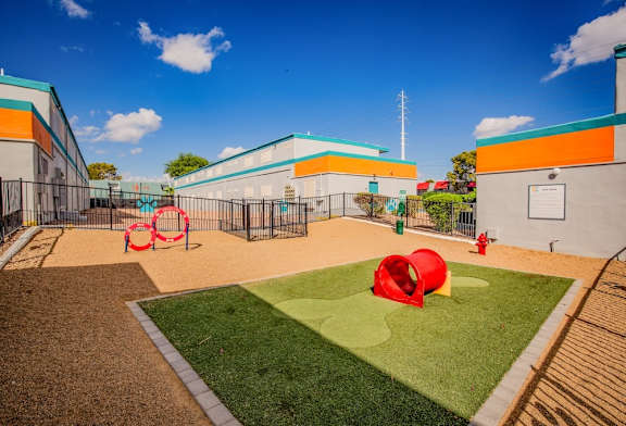 A dog park with a red tunnel and a green lawn.