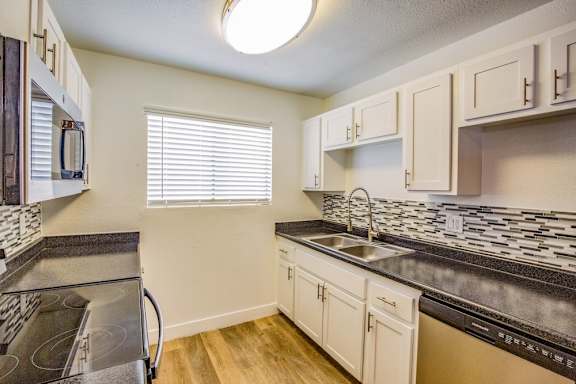 Kitchen in Fifteen 50 apartments in Las Vegas with dishwasher, electric stove, and shaker-style cabinets.