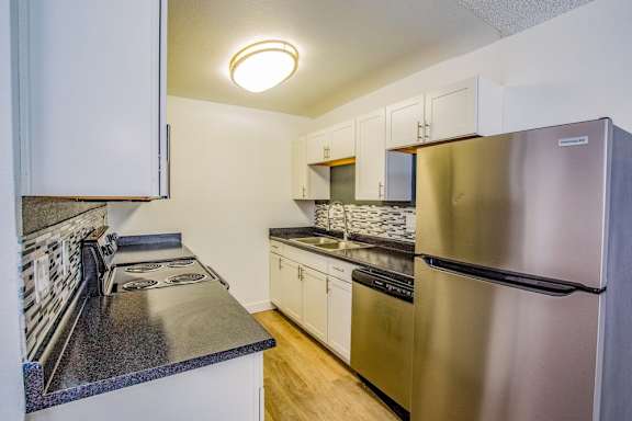 A kitchen with a stainless steel refrigerator and a black countertop.