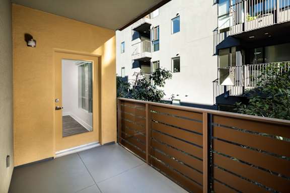 A balcony with a wooden railing and a glass door leading to a building.