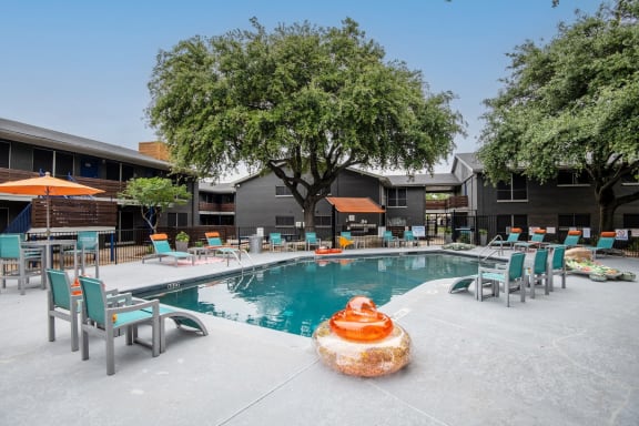 Community swimming pool at Stadium 700 luxury apartments in Arlington, TX with pool floats and a large tree.