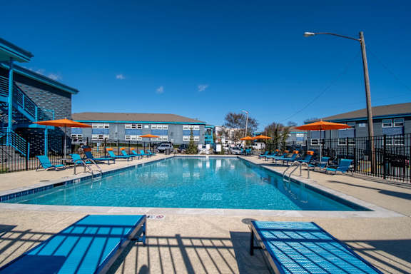 A large outdoor swimming pool at The Canvas Apartments Nashville with blue loungers and a clear blue sky.