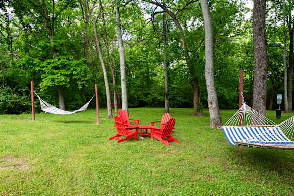 A red chair and a blue and white striped hammock are set up in a grassy area with trees in the background at the Retreat at Indian Lake Apartments in Hendersonville TN.
