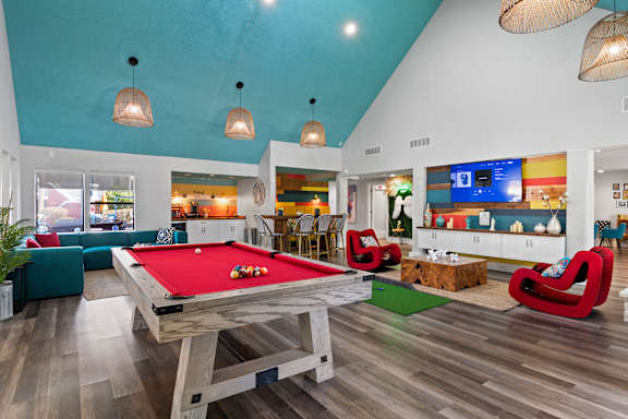 A pool table is in the middle of a room with a TV and a bar at the clubhouse at Fusion Orlando furnished apartments.