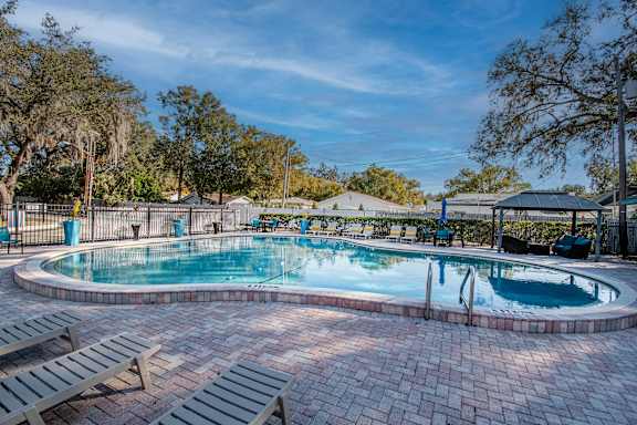 A swimming pool surrounded by trees and benches at Watermarc Apartments Lakeland, FL