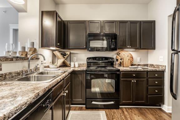 Indianapolis, IN Apartments - The Fort - Gourmet Kitchen with Dark Cabinets, Granite-Style Countertops, and Black Appliances.