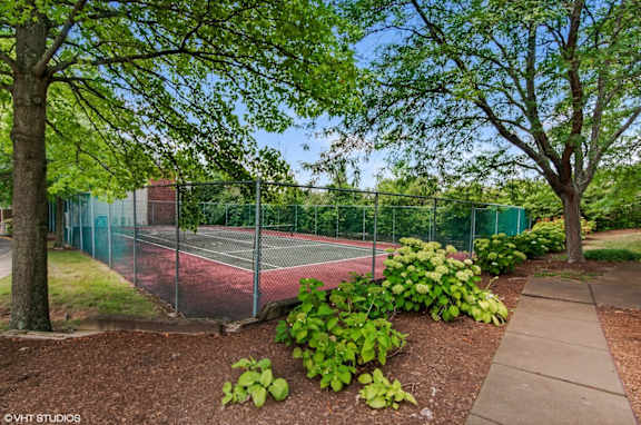 A tennis court is surrounded by a green fence and trees.