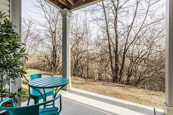 A green table and chairs on a porch with trees in the background.