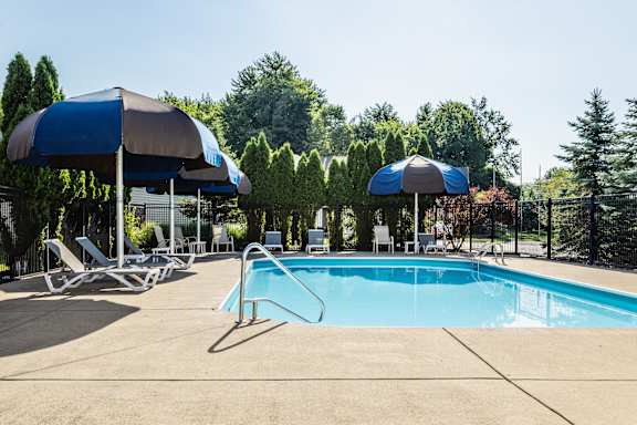 A swimming pool with a blue umbrella and lounge chairs.
