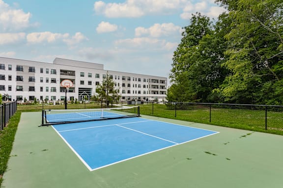 A blue tennis court is surrounded by a black fence and a white building.